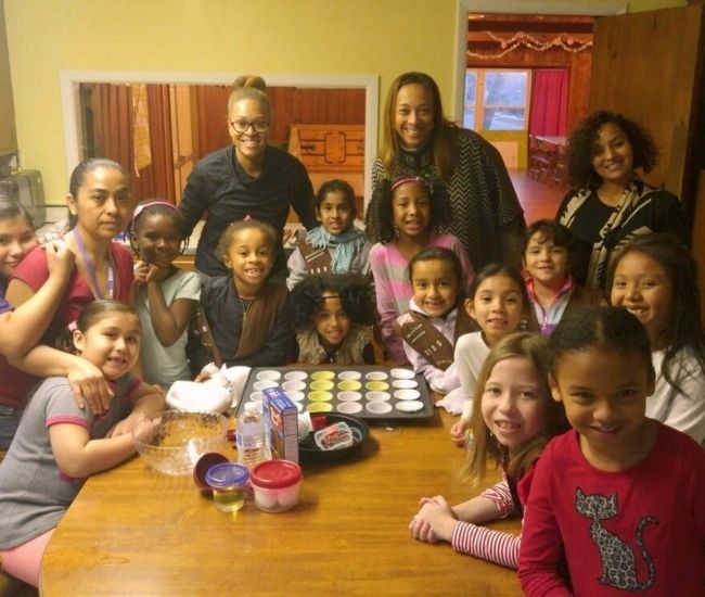 Brownie troop of 10-15 girls and adults gathered around a table with baking tools in front of them